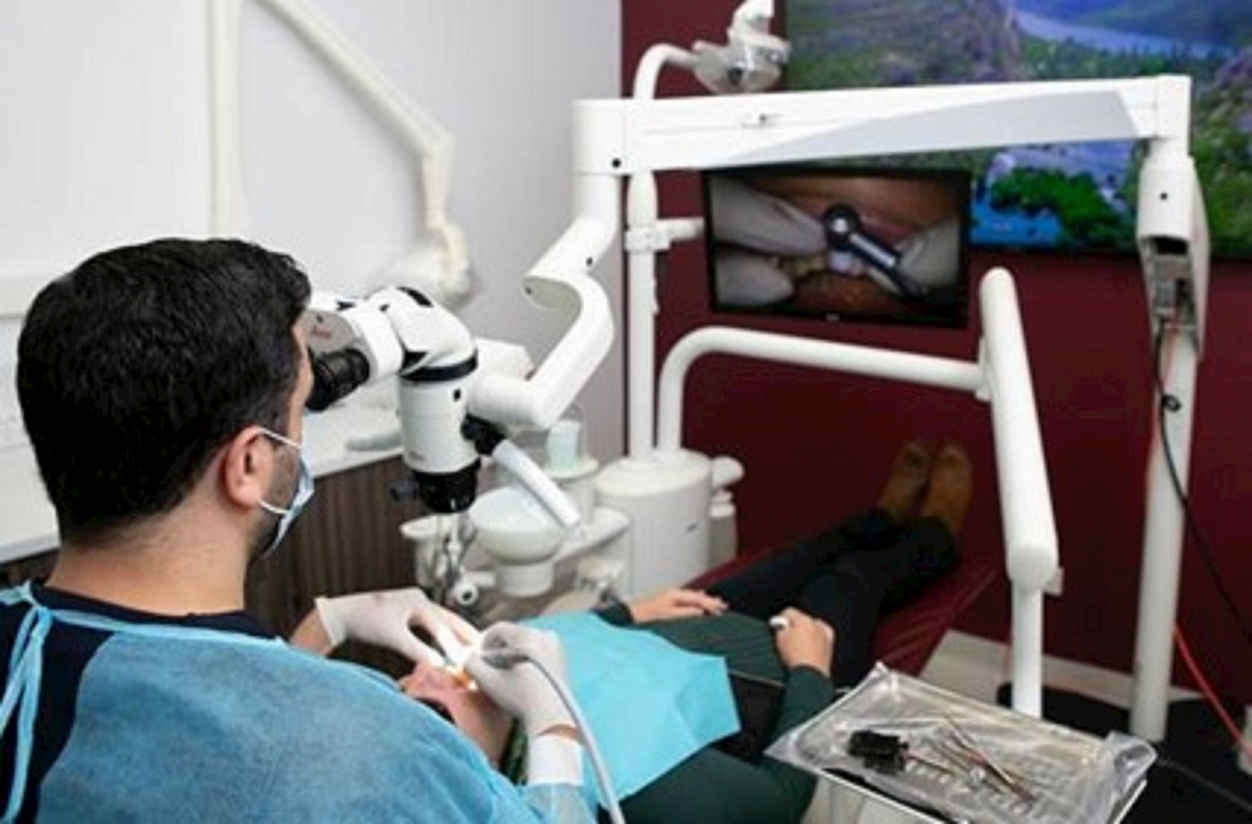 Dentist working through an operating microscope, with the intraoral field displayed on a monitor